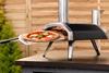 Four à pizza de marque Ooni, illustré dans un jardin avec une pizza à l'intérieur