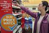 Woman shopping in Sainsburys next to an Aldi Price Match sign