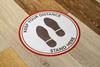 Social distancing sign on wooden floor that reads: 'Keep your distance. Stand here.'