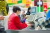 Out-of-focus checkout worker seen from behind with till in focus against a background of shoppers in store