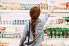Woman from behind shopping in supermarket dairy aisle, reaching up for bottle