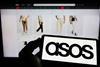 Hand in foreground holding phone with Asos logo. Asos website in background