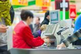 Out-of-focus checkout worker seen from behind with till in focus against a background of shoppers in store