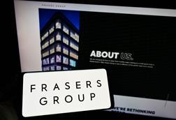 Frasers Group logo on a phone in front of a computer showing Frasers Group website
