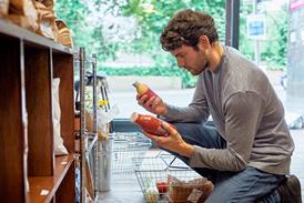 Man kneeling down in supermarket comparing prices of two drinks