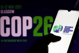 COP26 logo in background and a hand holding a phone with the same logo and the words: 'UN Climate Change Conference UK 2021'