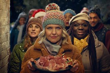 Waitrose Christmas ad still showing actress Ashley Jensen holding a plate of cold meat cuts in front of some carol singers