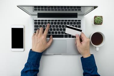 Person typing on laptop while holding credit card taken from above, with phone and coffee alongside
