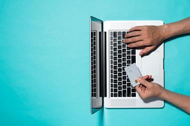 Photo taken from above of a person using a laptop and holding a bank card on a blue background