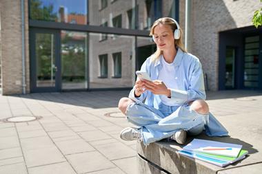 Student sitting outside on campus using smartphone