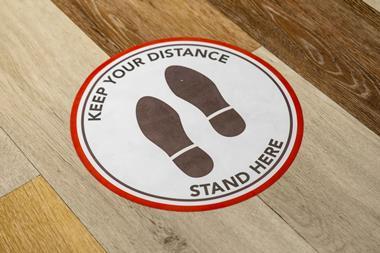 Social distancing sign on wooden floor that reads: 'Keep your distance. Stand here.'