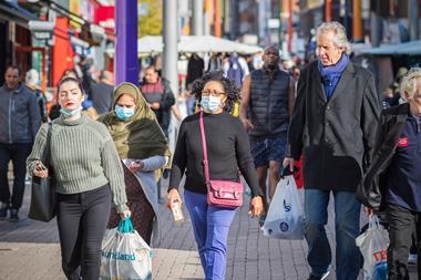 People wearing face masks walking down a street with market in the background