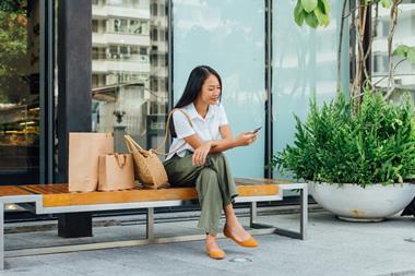 Woman sitting on bench outside store with shopping bags