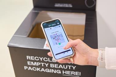 Marks & Spencer in-store beauty recycling bin behind customer holding a phone showing offers