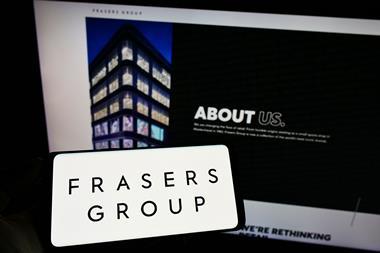 Frasers Group logo on a phone in front of a computer screen showing logo