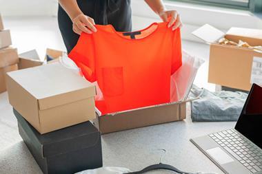 Woman shown from the head down packaging up clothing next to a laptop