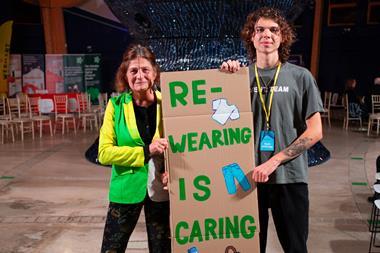 Two people holding up a sign that says 'Re-wearing is caring' at Eden Project fashion show for Anthropy