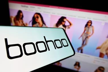 Boohoo logo on a phone held in front of a website showing female models in Boohoo clothing