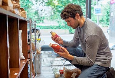 Man kneeling down in supermarket comparing prices of two drinks