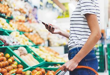 Female shopper in supermarket with basket, shown from head down