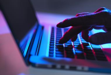 Hand typing on laptop keyboard at night