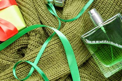 Styled image of a green bottle of perfume and green jumper with Christmas ribbons