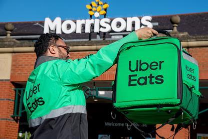 Uber Eats rider holding delivery bag outside Morrisons store