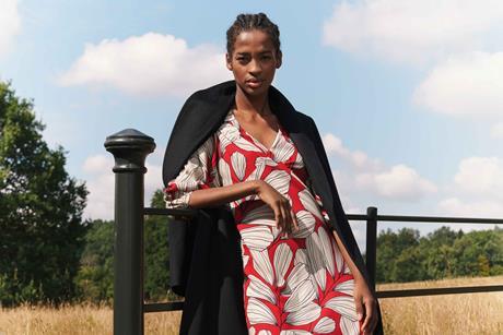 Black female model posing in red Jaeger for M&S dress against a gate outdoors