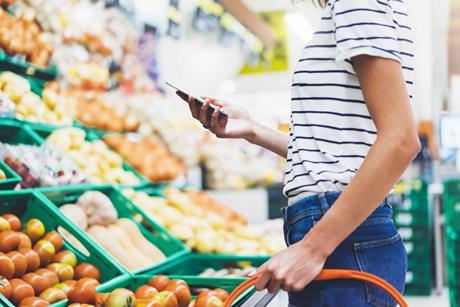 Female shopper in supermarket with basket, shown from head down