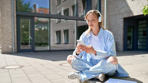 Student sitting outside on campus using smartphone