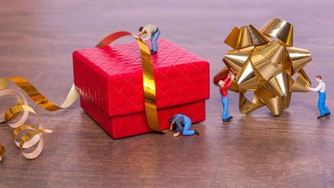 Toy-figures-wrapping-up-an-oversized-Christmas-present-with-ribbons