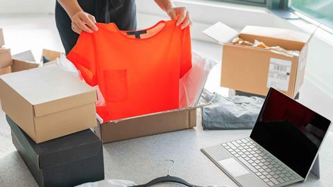 Woman shown from the head down packaging up clothing next to a laptop