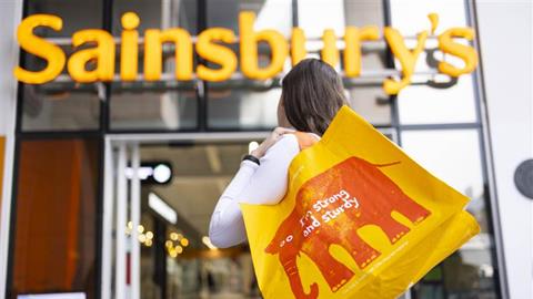 Woman holding Sainsbury's reusable bag and heading into Sainsbury's store