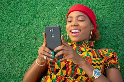 Young black woman lying on grass reading phone and smiling
