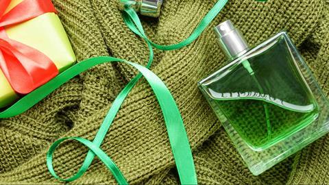 Styled image of a green bottle of perfume and green jumper with Christmas ribbons