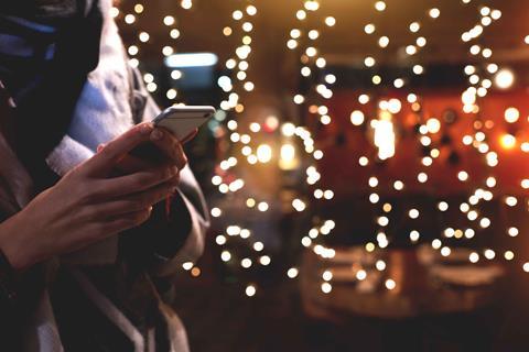 Woman-holding-mobile-phone-against-background-of-Christmas-lights-index