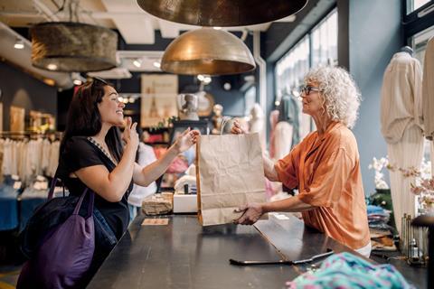 Store worker giving bag to happy customer at checkout in clothing store