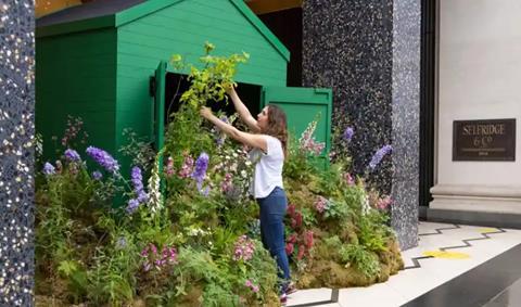 Woman arranging flowers outside green shed at Selfridges gardening centre