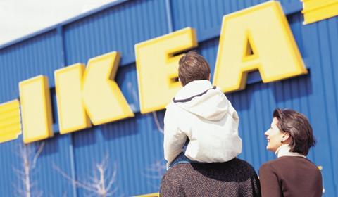 Exterior of Ikea store with a young family walking past, including a child on an adult's shoulders